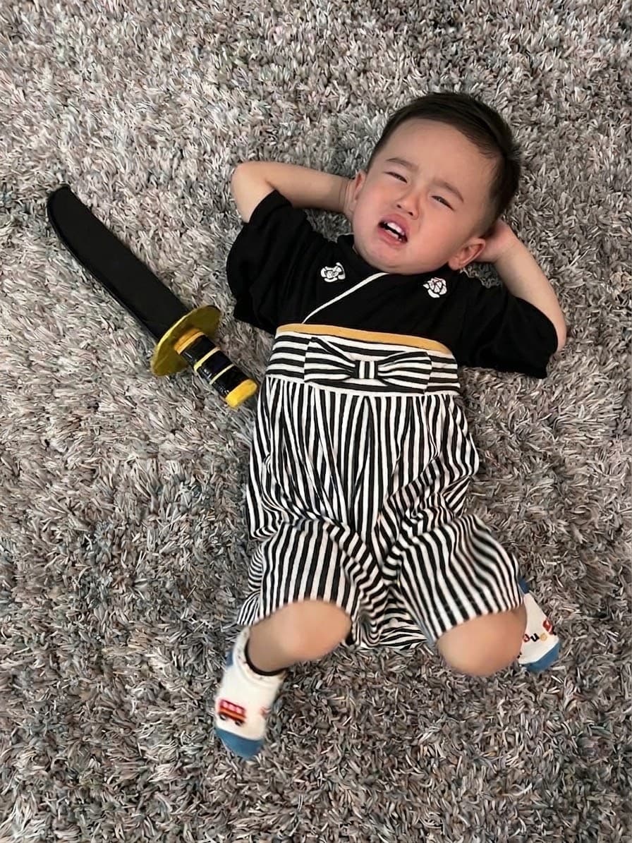 袴風の服を着て、床に寝転んで泣いている2歳くらいの男の子