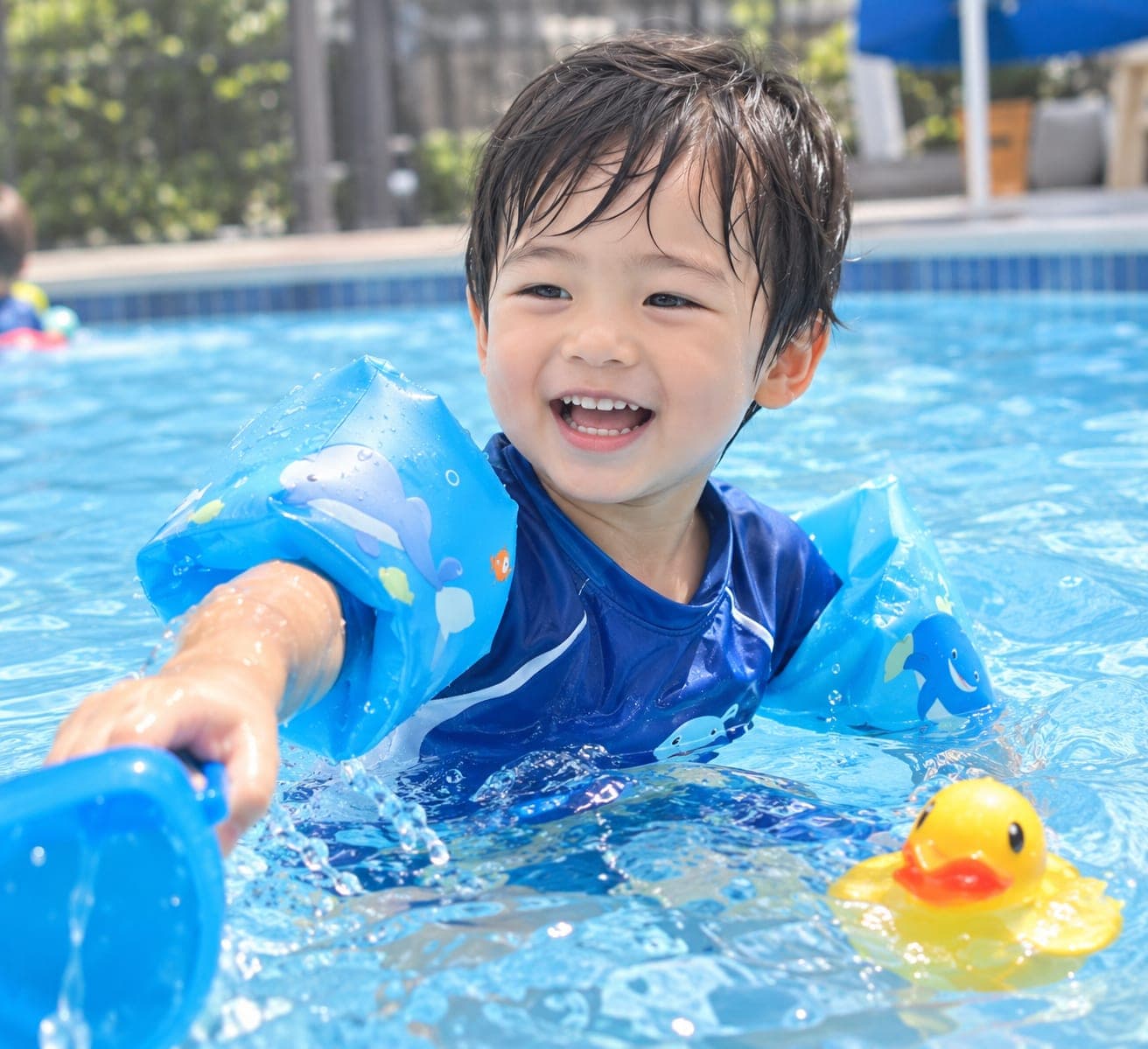 腕に浮き輪をつけてプールで笑顔で遊ぶ男の子