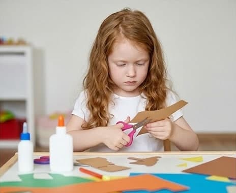 ハサミで色画用紙を切りながら、集中して工作に取り組む女の子