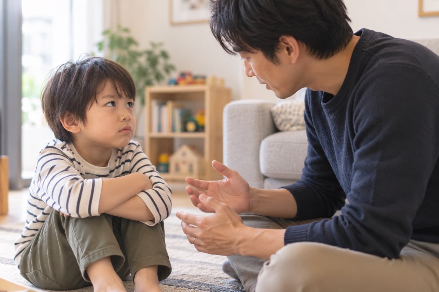 腕を組んでむくれている男の子に、お父さんが向き合って話しかけている様子