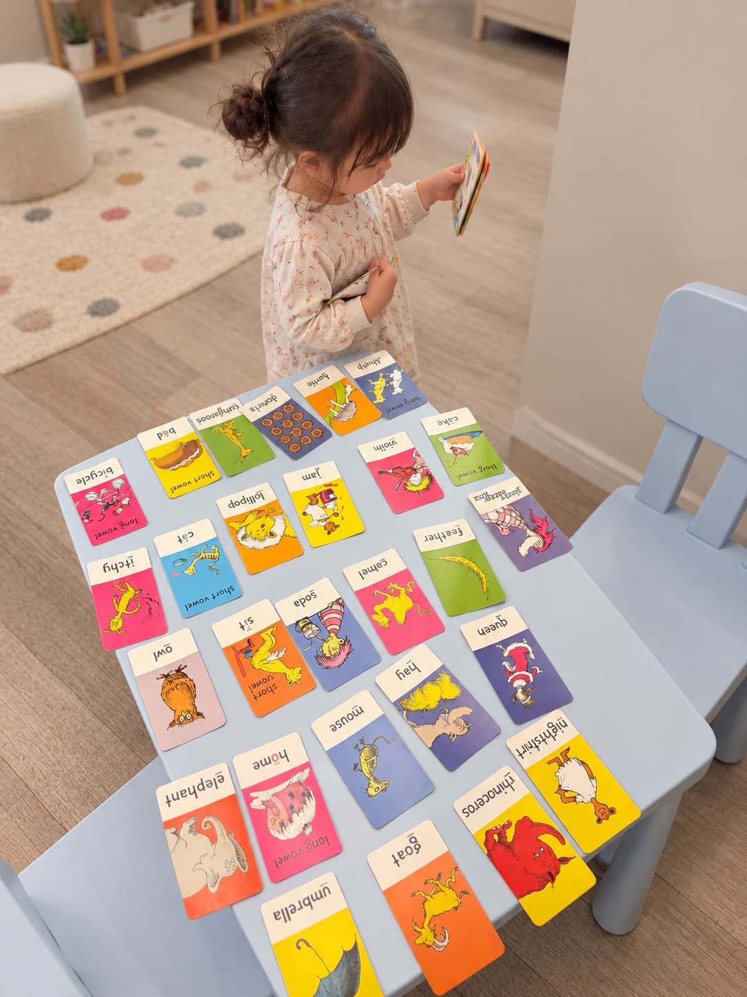 英単語と絵のカードをテーブルに並べて、絵本を手に見ている女の子