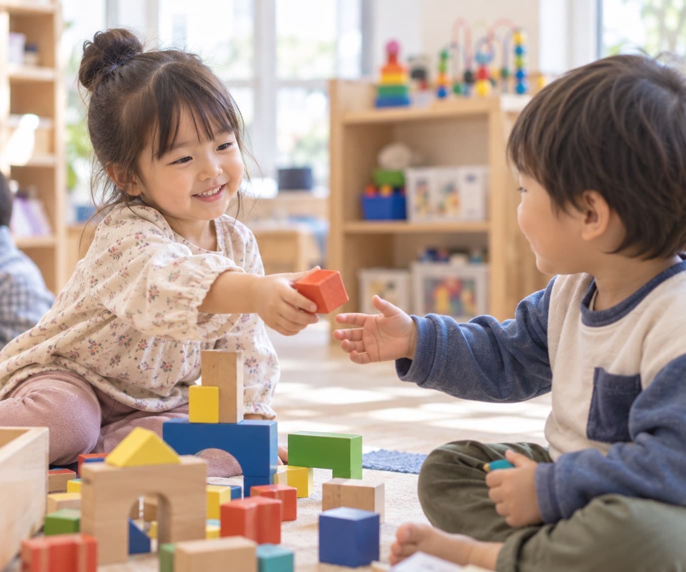 積み木のブロックを、笑顔で友だちに「どうぞ」と手渡している女の子