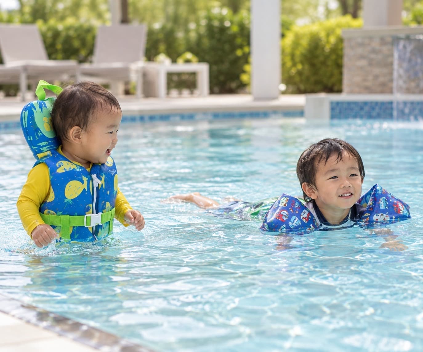 救命胴衣や腕の浮き具をつけて、プールで楽しそうに遊ぶ2人の子ども